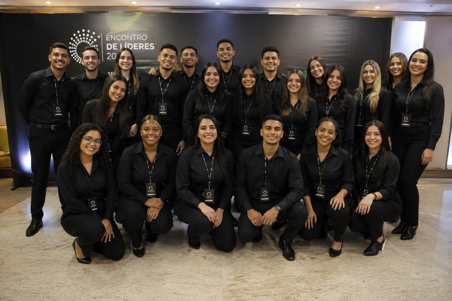 Equipe de recepção do Grupo INAC posando no credenciamento de um congresso, toda de preto e com crachá